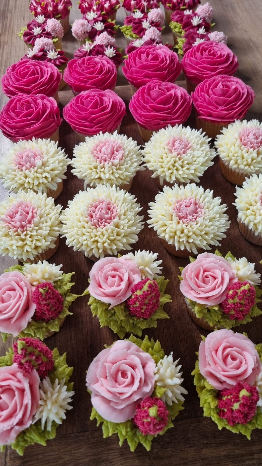 Rows of floral cupcakes piped as pink roses and chrysanthemums